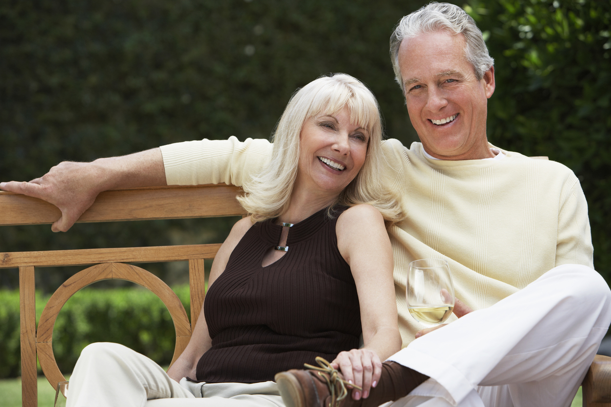 Happy middle aged couple sitting on bench with wine glass in the Garden ...